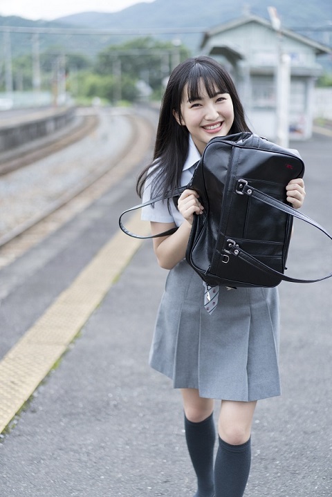 駅のホームでグレーの制服に身を包み微笑むHKT48の田島芽瑠
